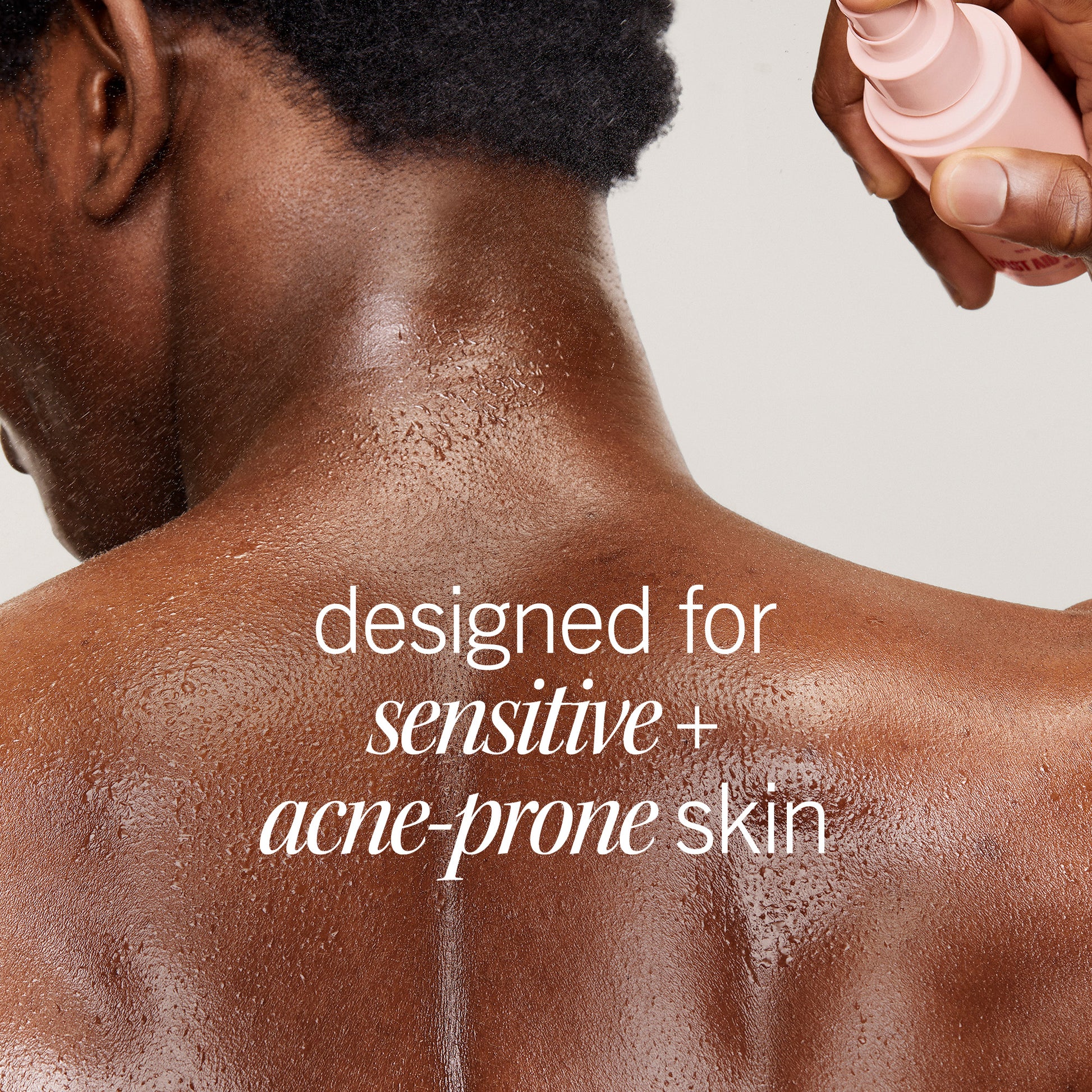 A person with damp skin has a pink spray bottle applied to their back. The text reads: “designed for sensitive + acne-prone skin.” The background is plain, emphasizing the action.