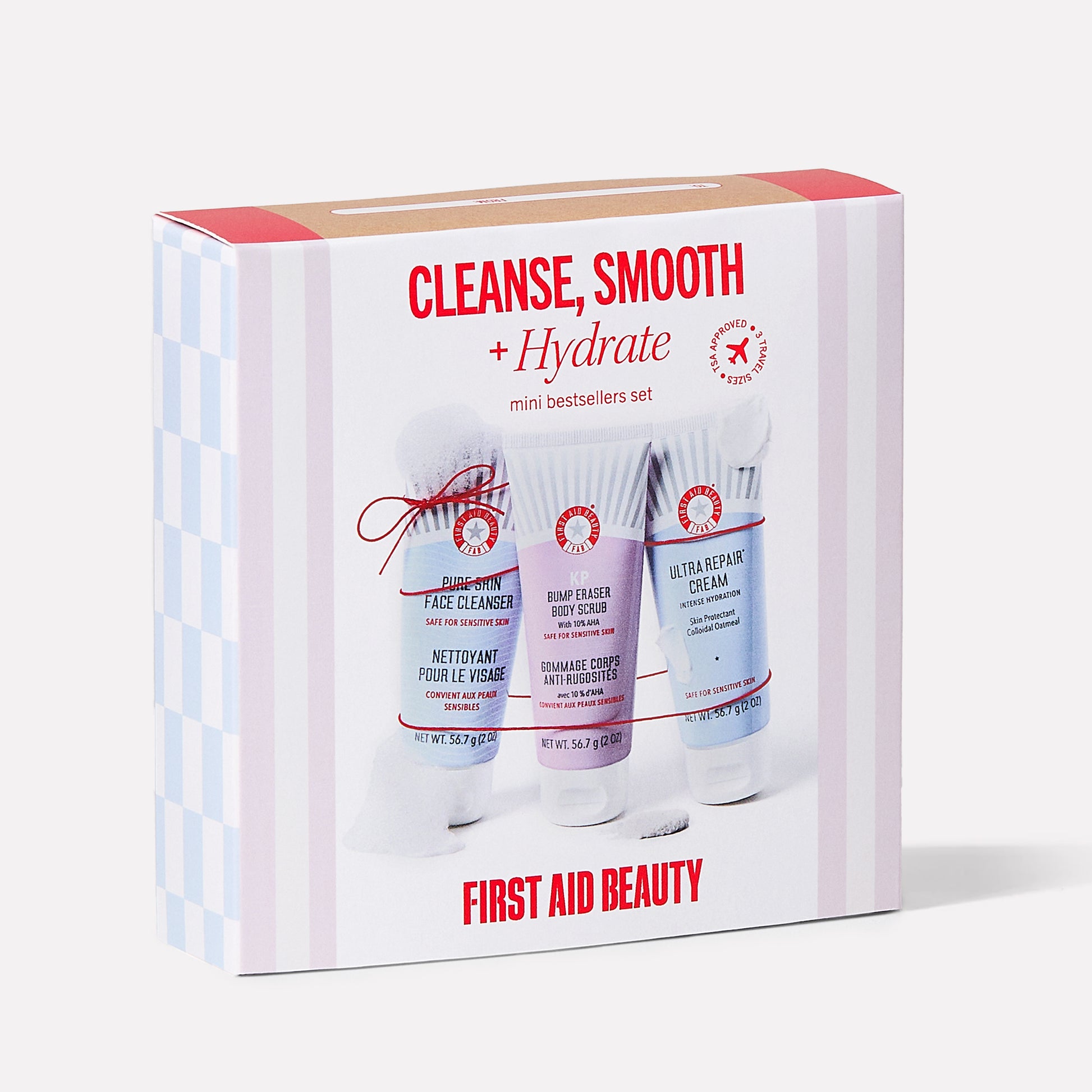 The box contains three skincare products labeled "Pure Skin Face Cleanser," "KP Bump Eraser Body Scrub," and "Ultra Repair Cream." Text: "CLEANSE, SMOOTH + Hydrate mini bestsellers set," "FIRST AID BEAUTY."