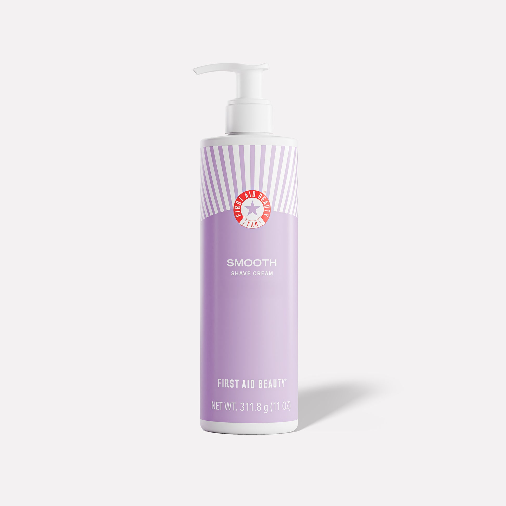 A lavender bottle with a pump, labeled "First Aid Beauty Smooth Shave Cream," stands against a plain backdrop. The text includes "NET WT. 311.8 g (11 oz)."