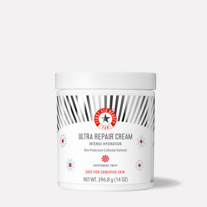 A white jar labeled "First Aid Beauty Ultra Repair Cream." It provides intense hydration with colloidal oatmeal, peppermint twist fragrance, safe for sensitive skin, 396.8 g (14 oz). Decorated with grey rays and snowflake patterns.